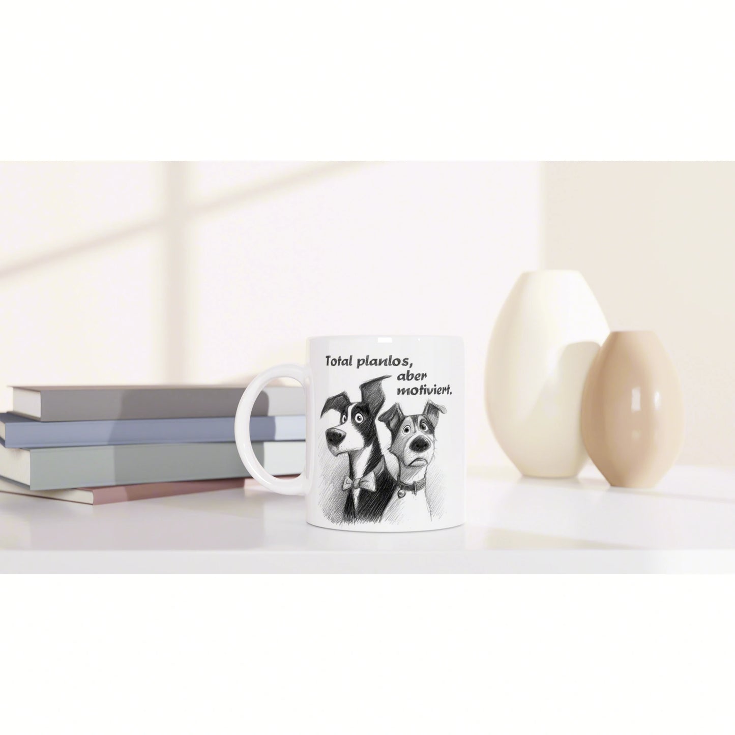 White mug with cartoon dogs and the German caption Total planlos, aber motiviert on a desk beside books and vases.