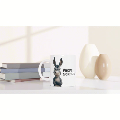 White mug mockup featuring a cartoon donkey and bold text, placed beside stacked books and decorative white and beige ceramic vases.