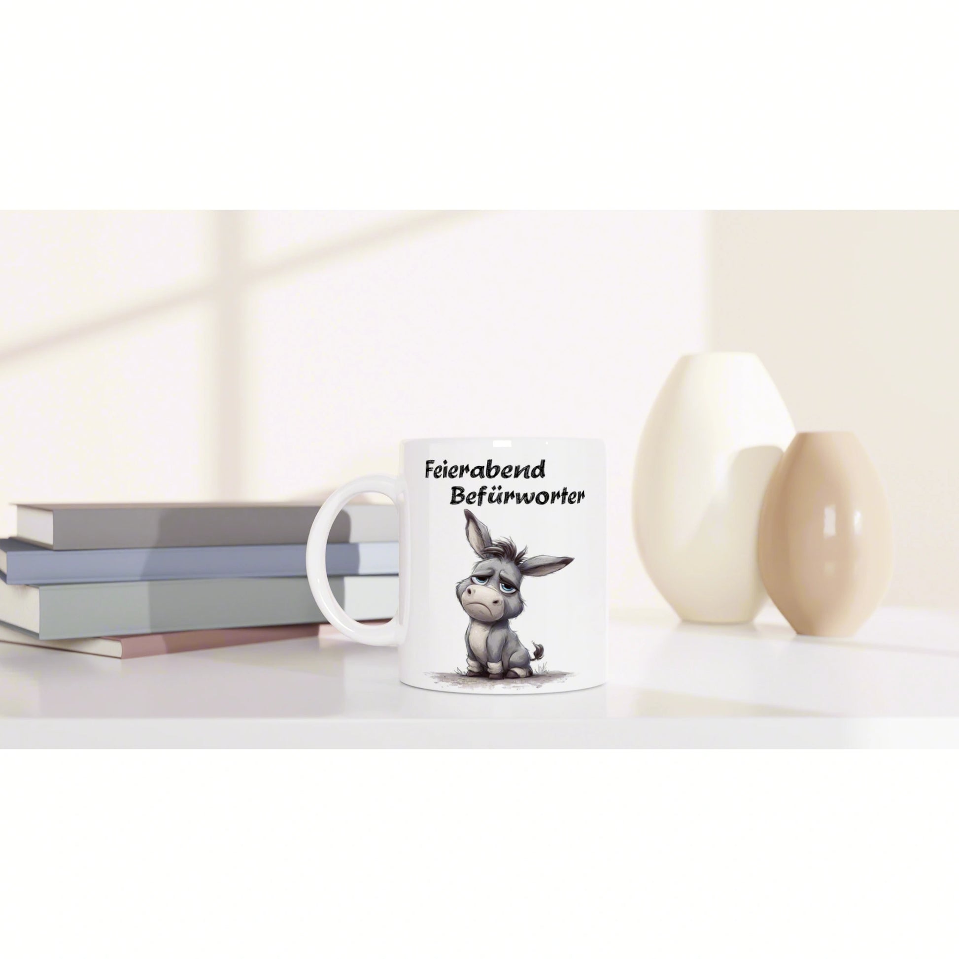 Product image: white mug with a sad cartoon donkey and the German phrase Feierabend Befürworter, beside stacked books and ceramic vases.