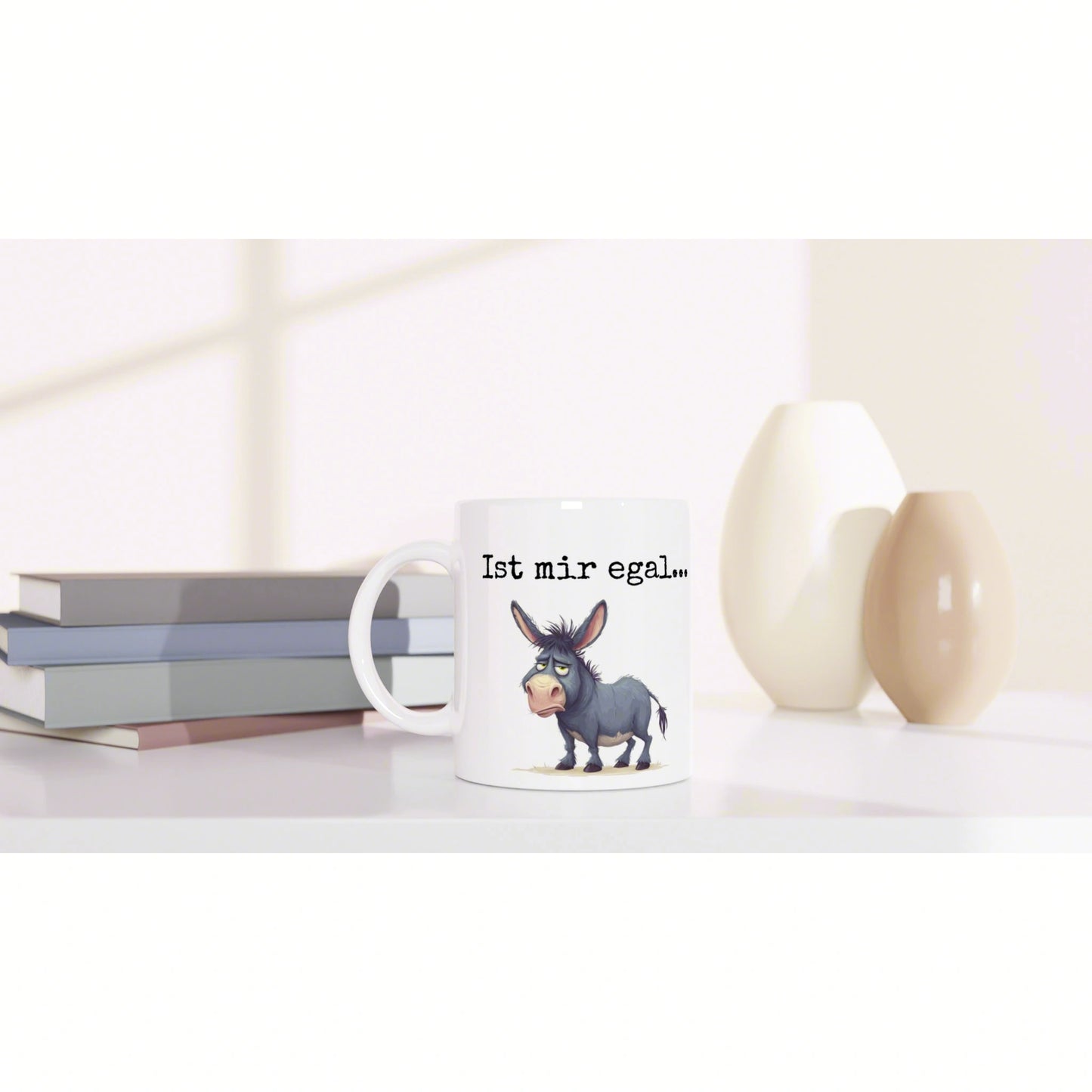 White mug with a cartoon donkey and the German phrase Ist mir egal, set on a desk with books and beige vases.