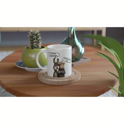 Product mockup: white mug with cartoon donkey and monkey and speech bubbles, on a wooden coaster beside plants.