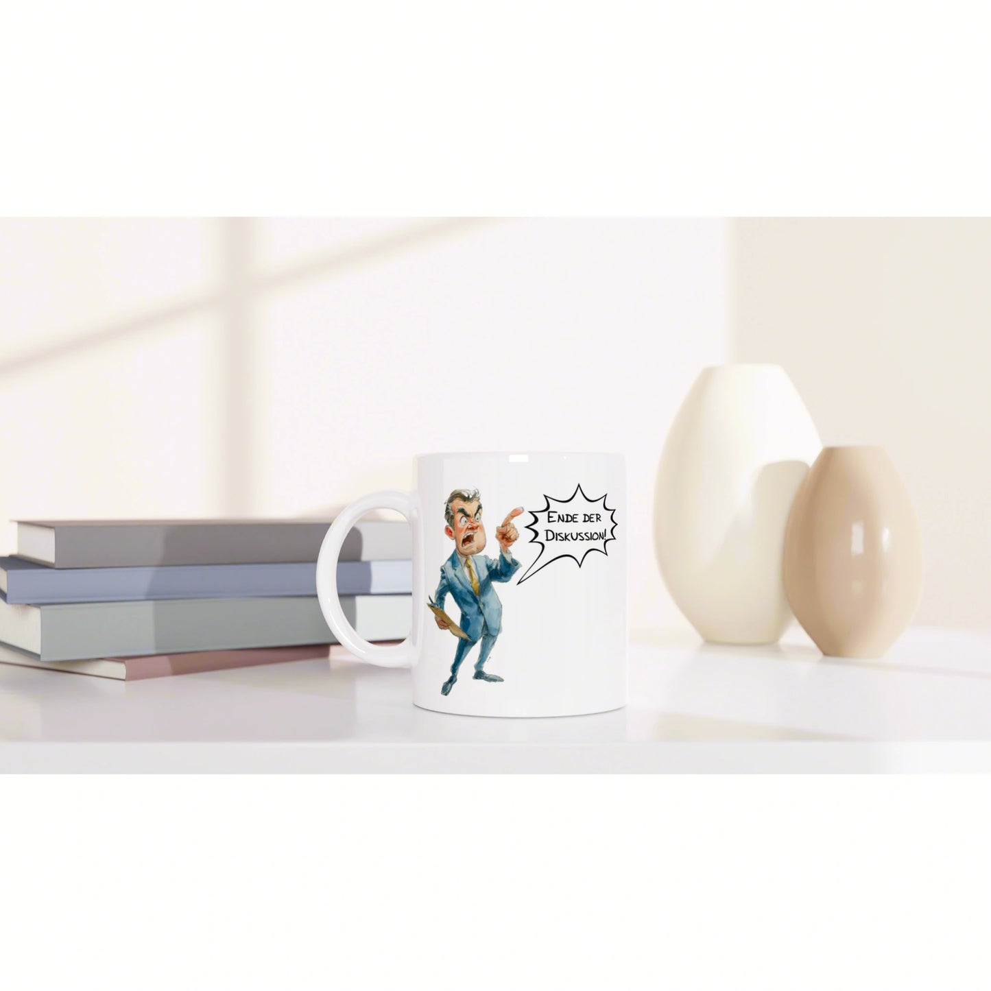 White ceramic mug featuring a cartoon man shouting 'Ende der Diskussion' on a desk beside stacked books and beige vases.