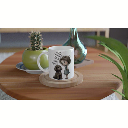 White mug on a wooden coaster features a cartoon girl talking to a dog; plant decor and cactus in the background.