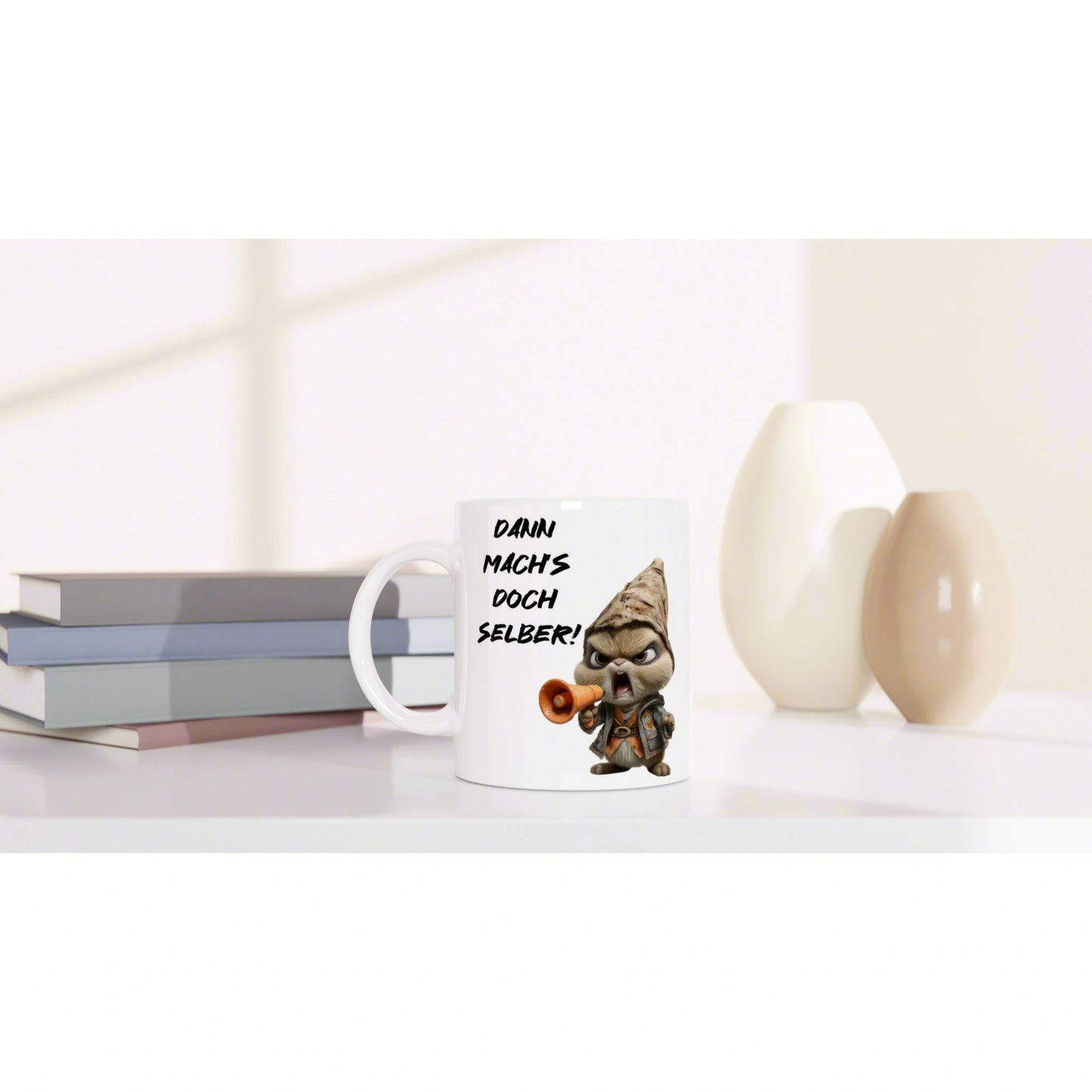 White mug with a cartoon gnome and megaphone, displaying the German slogan DANN MACHS DOCH SELBER!, on a desk with books.
