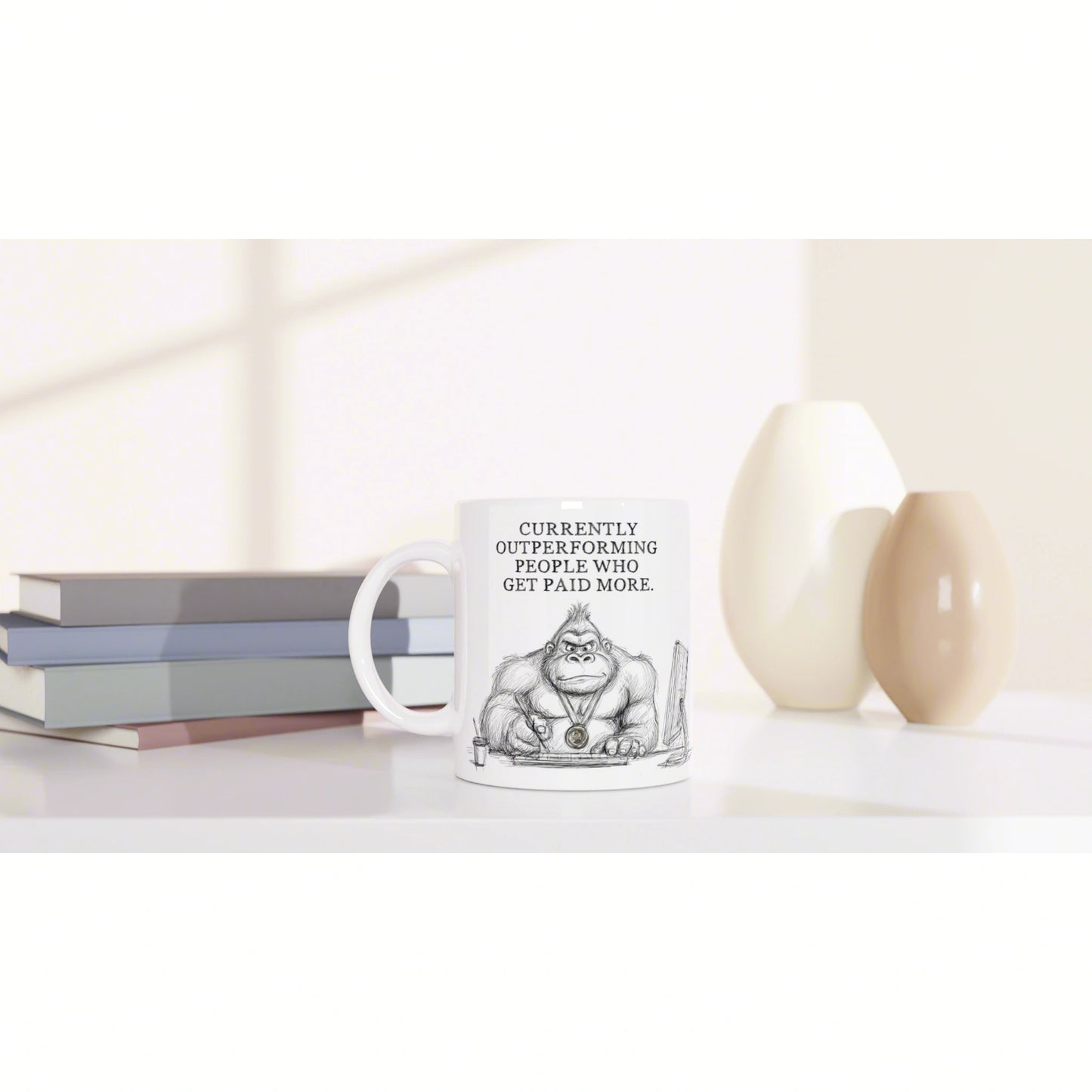 White mug with a cartoon gorilla and the slogan Currently outperforming people who get paid more, beside books and vases.
