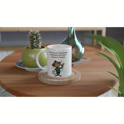 White mug with a cartoon monkey in a suit and a German champagne slogan, on a wooden table beside a cactus.