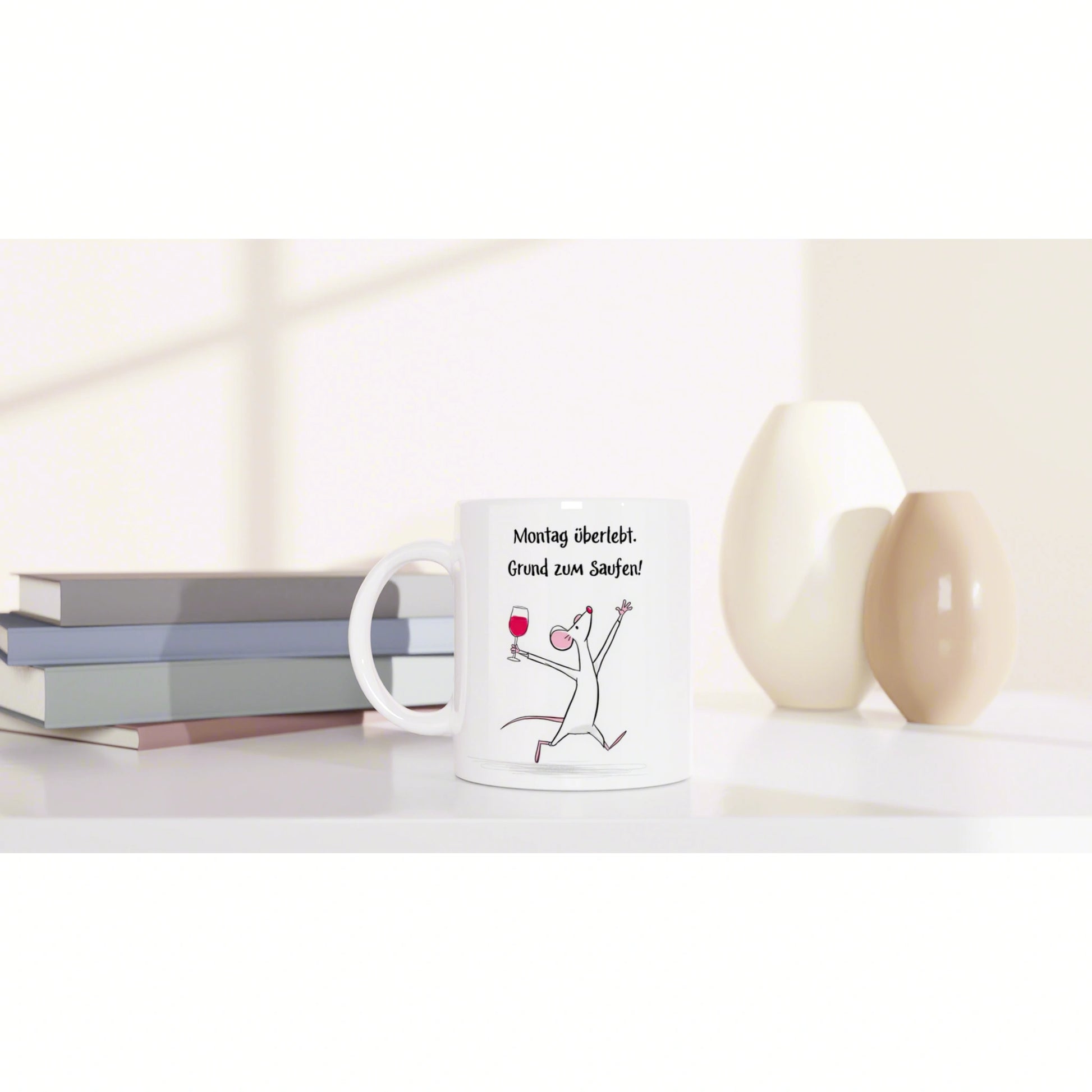 White mug featuring a cartoon mouse with a wine glass and a German slogan, beside books and vases.