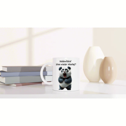 White mug featuring a cartoon panda and German caption Heidewitzka! Schon wieder Montag?! on a shelf beside books and vases.