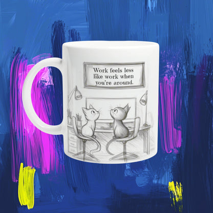 White mug with a pencil sketch of two cats at a desk and a framed quote: Work feels less like work when you're around.