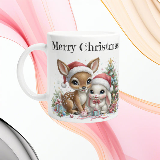 White mug featuring Christmas illustration of a fawn and bunny in Santa hats with gifts and a tree, 'Merry Christmas' text.
