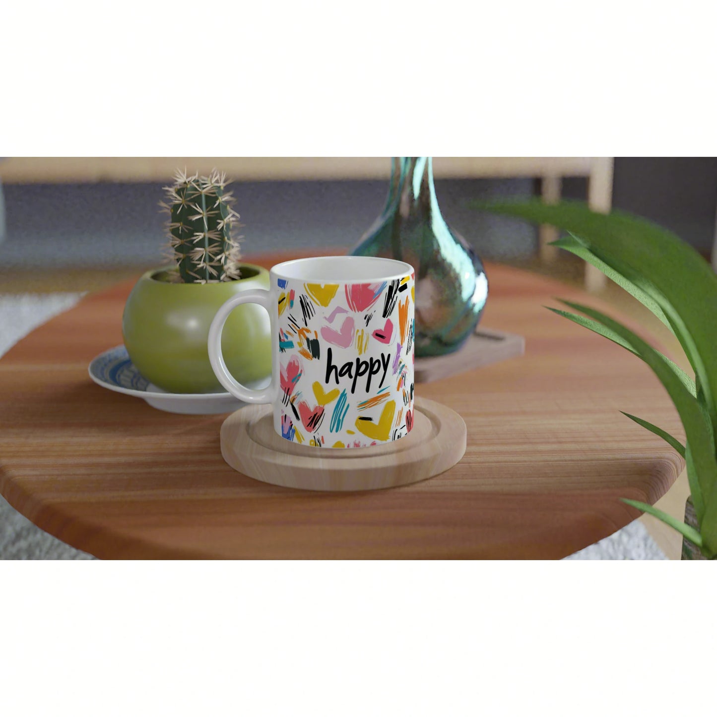 White mug with colorful abstract hearts and the word 'happy' on a wooden coaster, set on a table with plants.