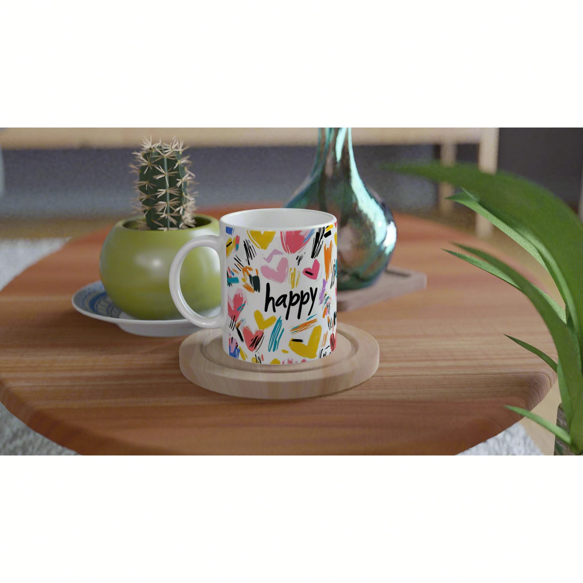 White mug with colorful abstract hearts and the word 'happy' on a wooden coaster, set on a table with plants.