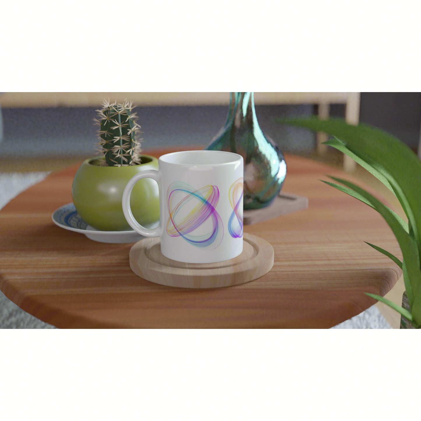White mug with colorful abstract loops sits on a wooden coaster on a coffee table, with a cactus and vase in the background.