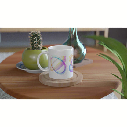 White mug with colorful abstract loops sits on a wooden coaster on a coffee table, with a cactus and vase in the background.