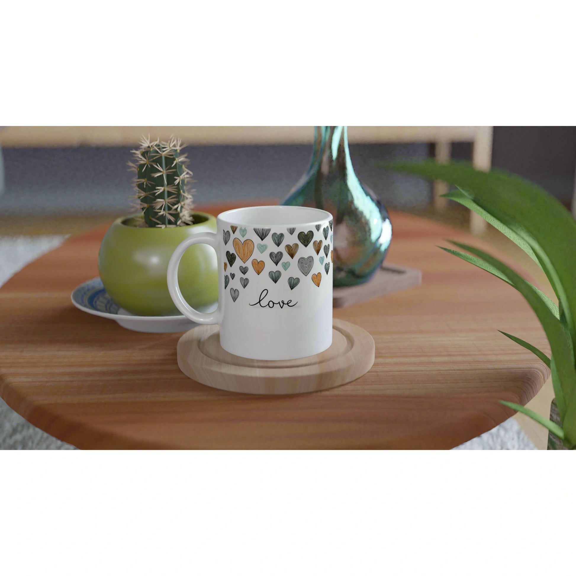 White mug with colorful hearts and the word love sits on a wooden table, with a cactus pot and teal vase in the background.