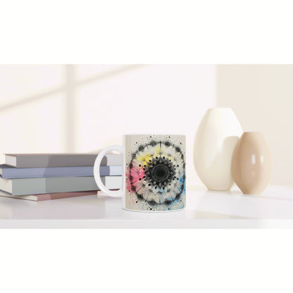 White mug with a colorful mandala floral design on a white shelf beside pastel books and ceramic vases—product mockup.