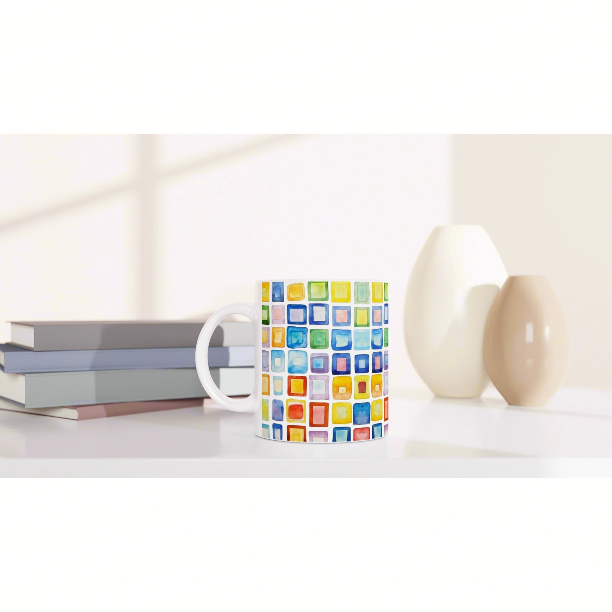 White mug featuring a colorful square mosaic pattern, placed on a shelf with stacked books and two ceramic vases.