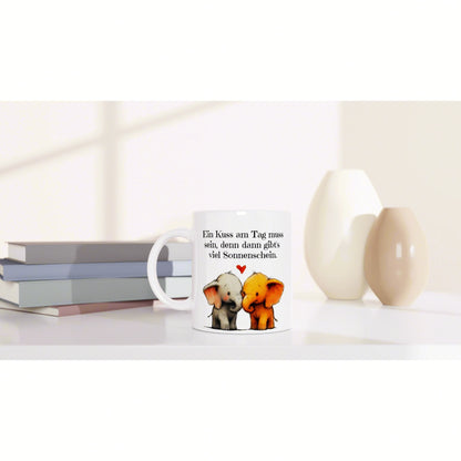 White mug featuring two elephants kissing with a heart and a German caption about a daily kiss and sunshine.