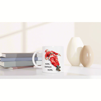 White mug featuring a falling Santa illustration and the words NOPE. EINFACH NOPE on a desk with books and decorative vases.