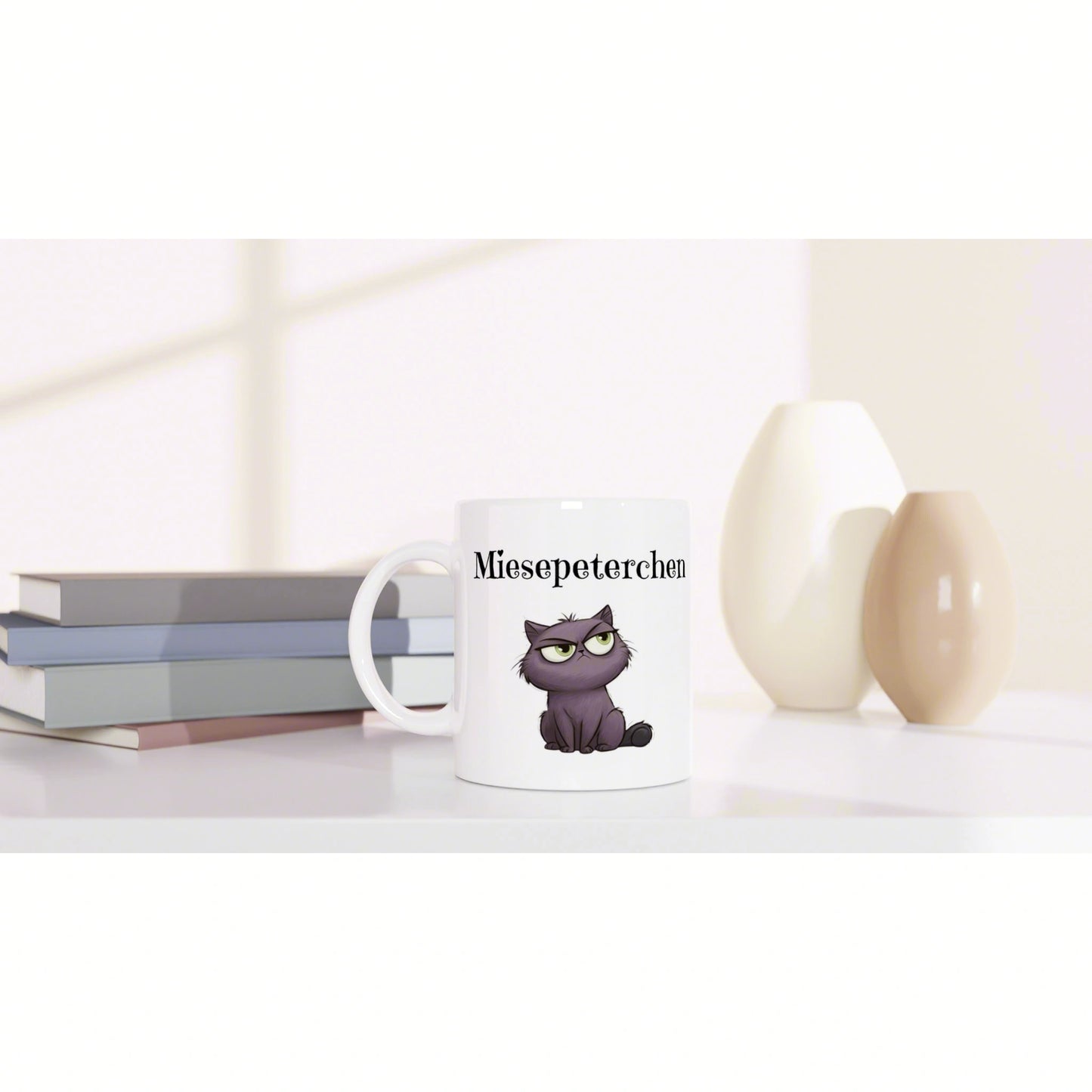 White mug featuring a purple cat illustration and the text Miesepeterchen, set beside books and decorative vases.