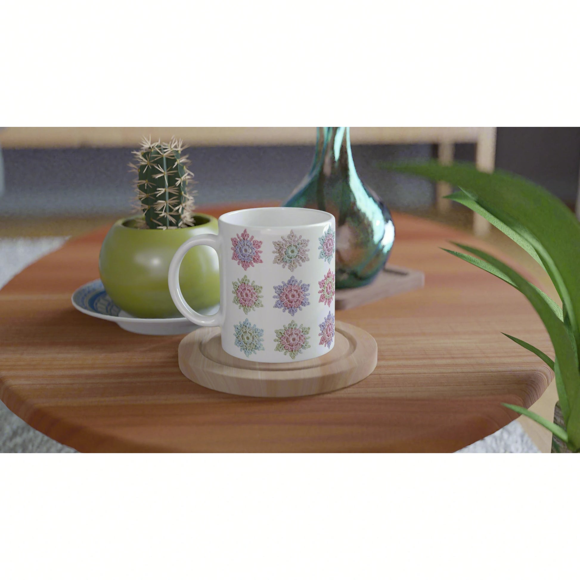 Product mockup: white mug with pastel floral pattern on a wooden coaster, on a wooden table with cactus and decorative vase.