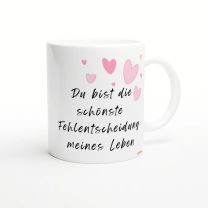 White mug with black cursive German quote 'Du bist die schönste Fehlentscheidung meines Lebens' and pink heart illustrations.