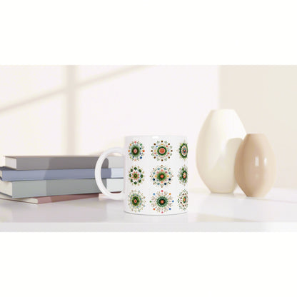 White mug with a repeating green floral medallion pattern, shown as a product mockup beside books and decorative vases.