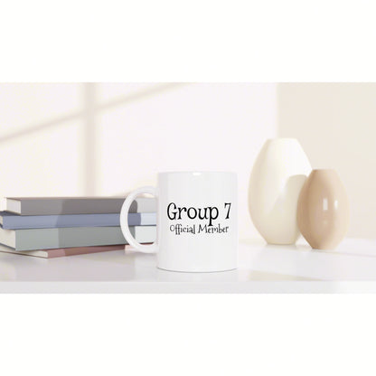 White mug with 'Group 7 Official Member' text on a shelf beside stacked books and decorative vases.