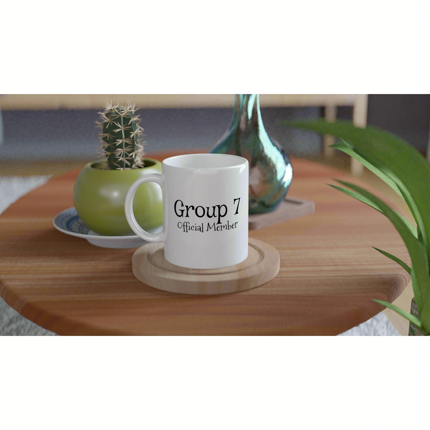 White mug on a wooden coaster with 'Group 7 Official Member' text, on a table beside a cactus pot and a turquoise vase.