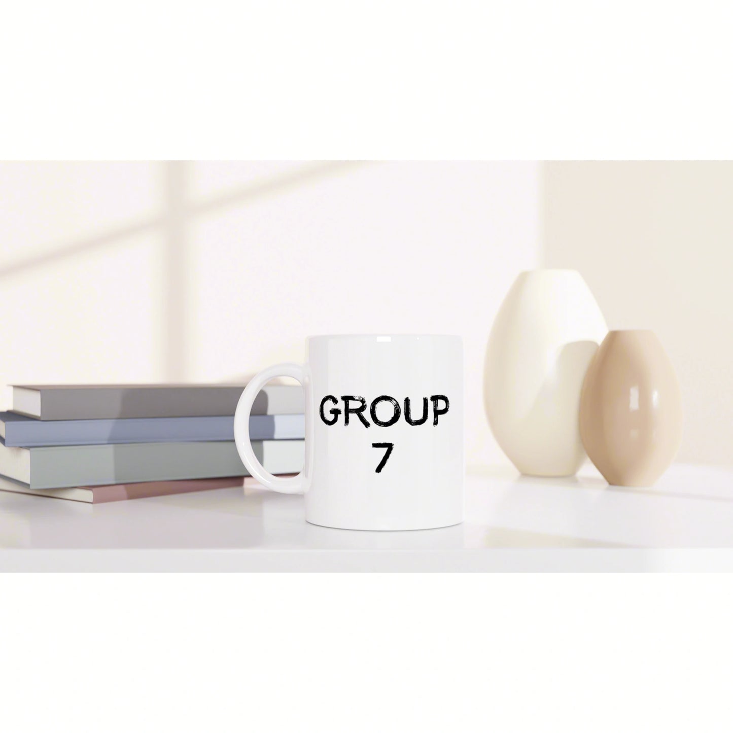 White mug with GROUP 7 printed, placed on a shelf beside stacked books and two decorative vases.