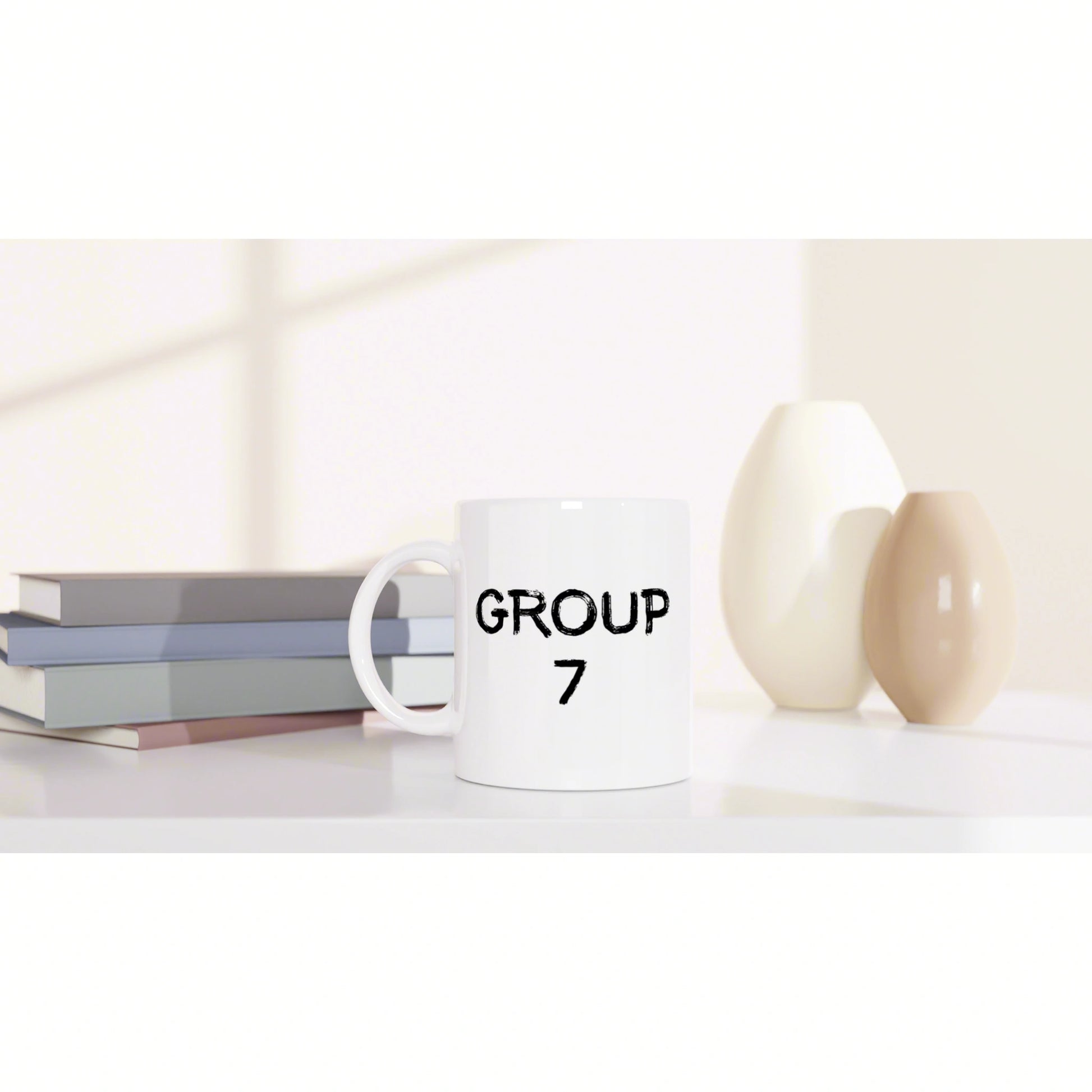 White mug with GROUP 7 printed, placed on a shelf beside stacked books and two decorative vases.