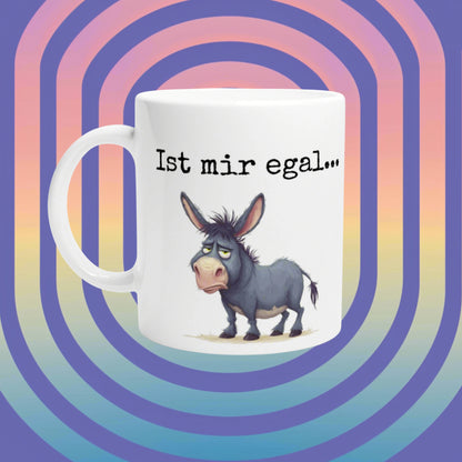 White mug with a grumpy cartoon donkey and the German caption 'Ist mir egal...' on a vibrant rainbow backdrop (product mockup).