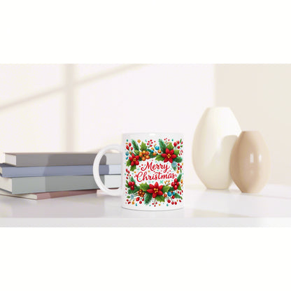 Product mockup: white mug with a colorful Merry Christmas floral design on a white surface, beside books and decorative vases.