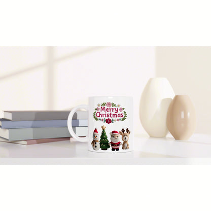 White mug with 'Merry Christmas' and knitted holiday characters, placed on a shelf beside pastel vases and stacked books.