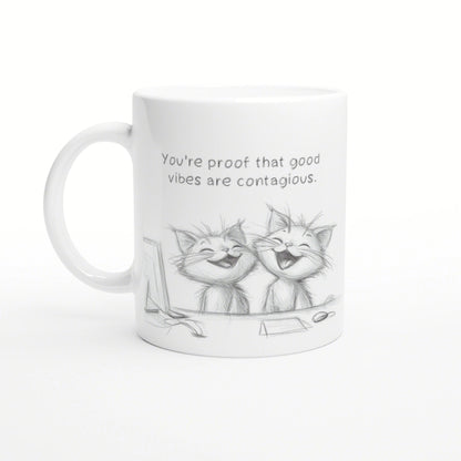 White mug mockup featuring a pencil sketch of two laughing cats and the slogan 'You're proof that good vibes are contagious.'