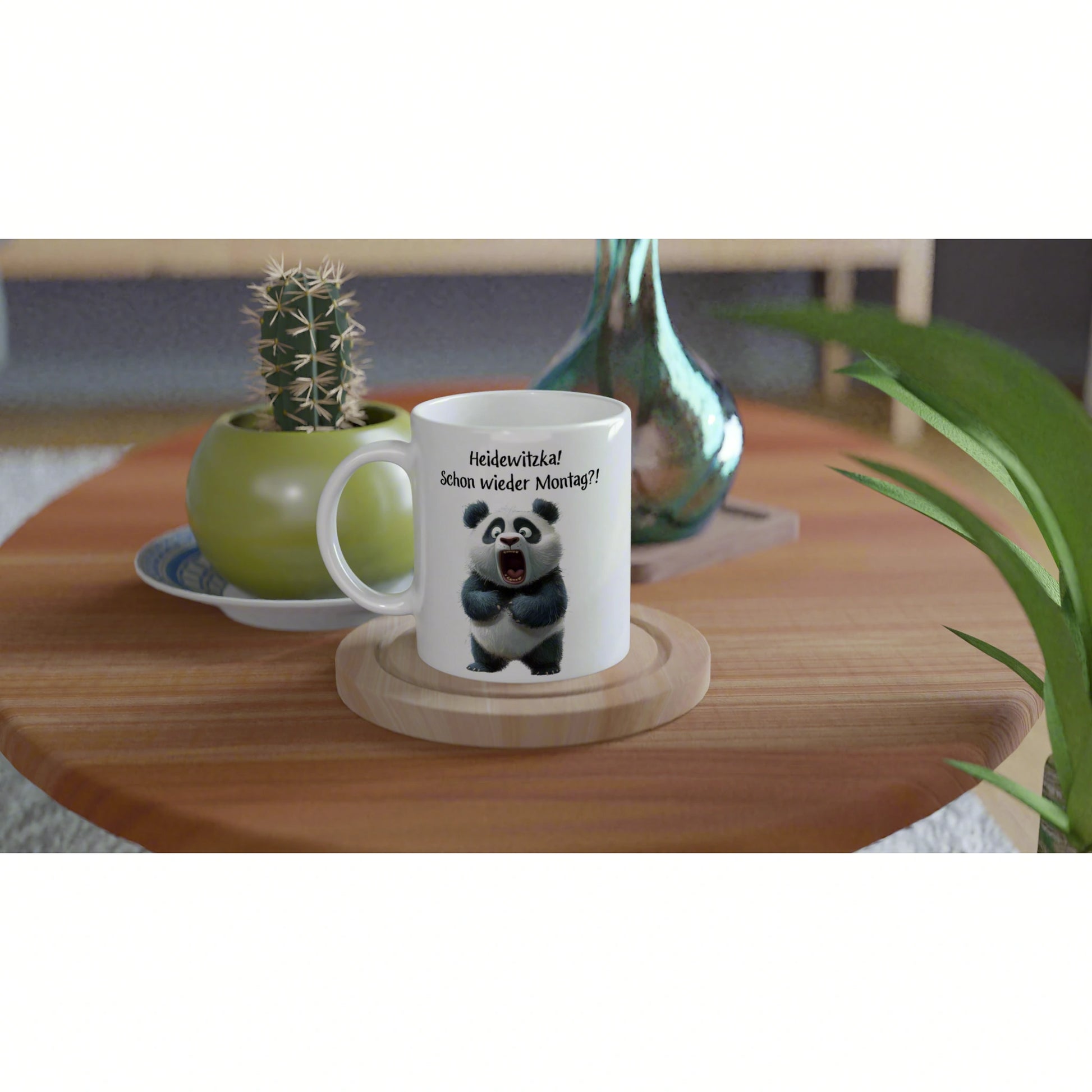 White mug with a panda cartoon and the caption 'Heidewitzka! Schon wieder Montag?!' on a wooden coaster, set on a table with plants in the background.