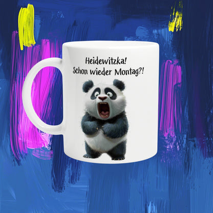 White mug mockup featuring a cartoon panda and the German slogan Heidewitzka! Schon wieder Montag?! on a blue background.