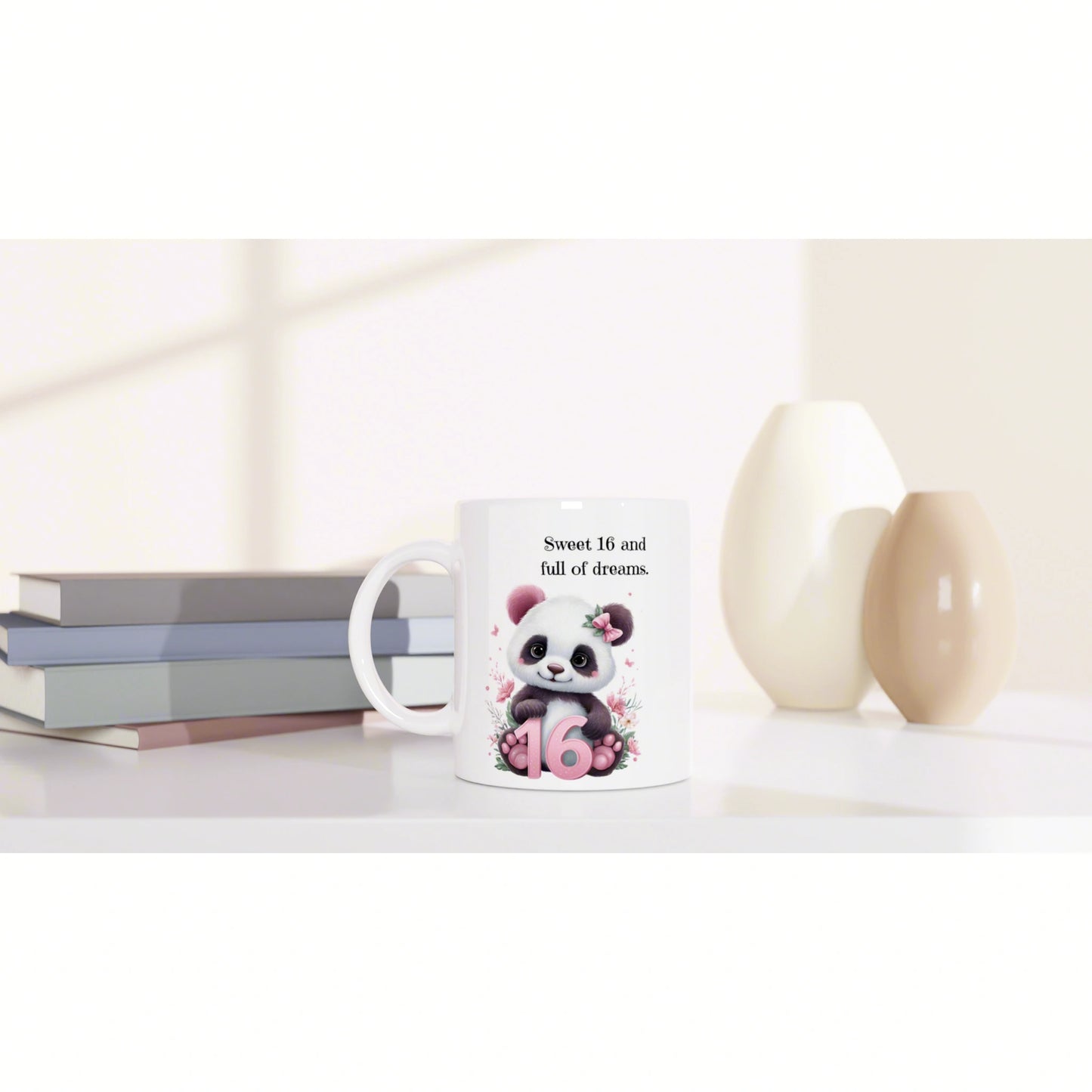 White mug featuring a panda and the phrase Sweet 16 and full of dreams, with a pink 16, beside books and decorative vases.