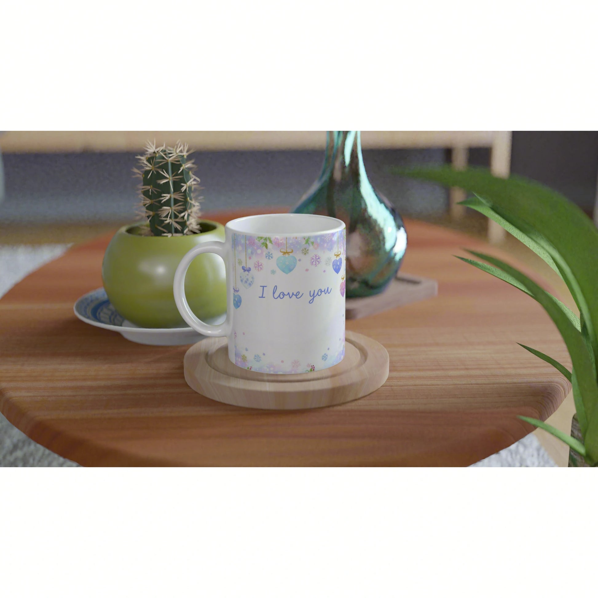 White mug with pastel heart decorations and I love you text on a wooden coaster, on a table with a cactus pot.