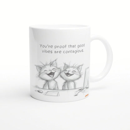 White mug featuring a pencil sketch of two laughing cats and the quote: You're proof that good vibes are contagious.