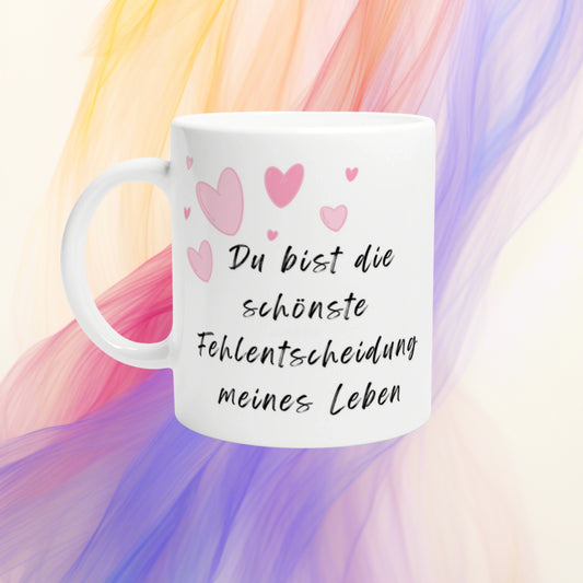 White mug with pink hearts and cursive German text Du bist die schönste Fehlentscheidung meines Lebens on pastel background.