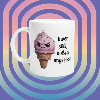 White mug featuring a pink ice-cream cone with an angry face and the German slogan Innen süß, außen angepisst on a pastel rainbow background.