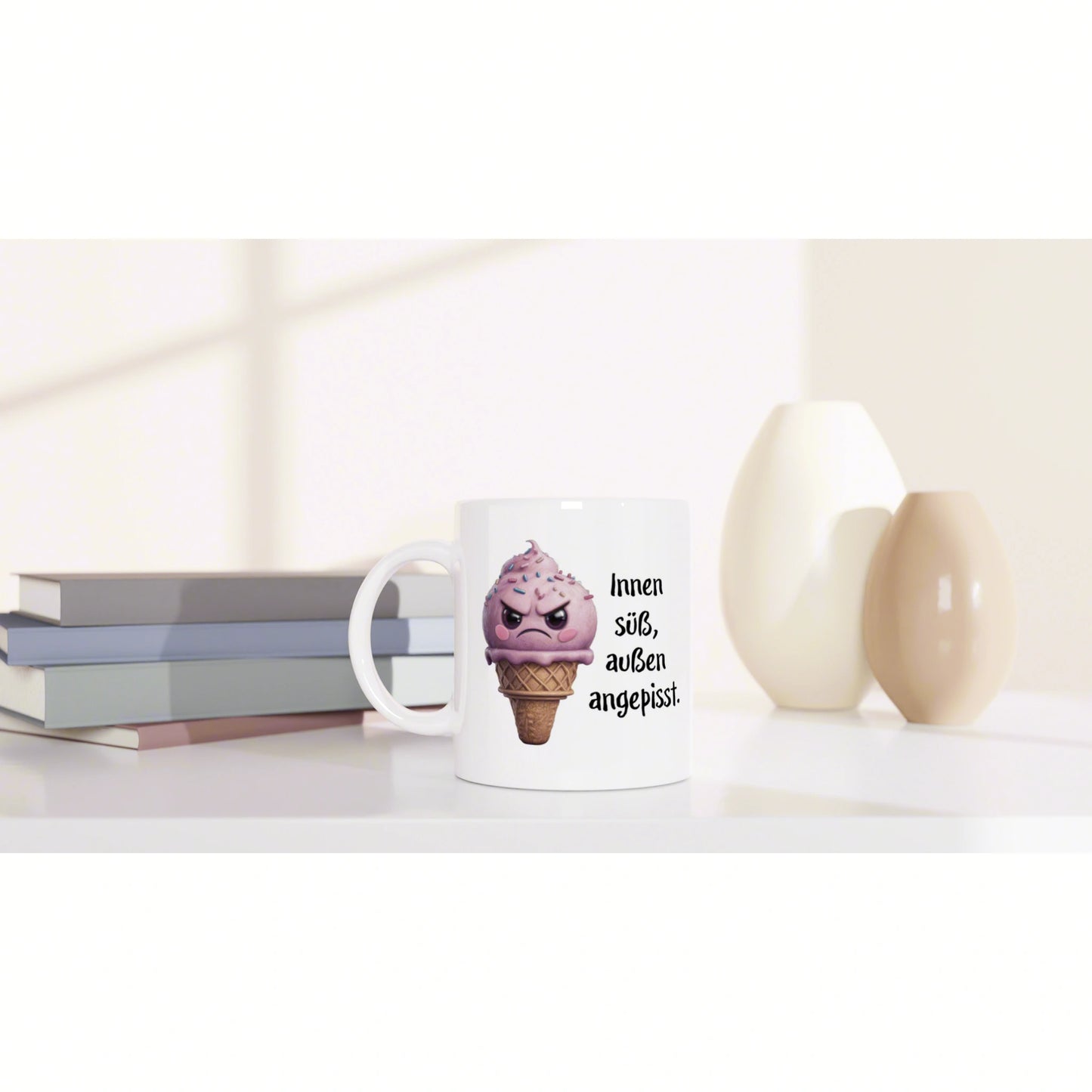 White mug featuring a pink ice-cream cone cartoon and German slogan 'Innen süß, außen angepisst' on a desk with books.