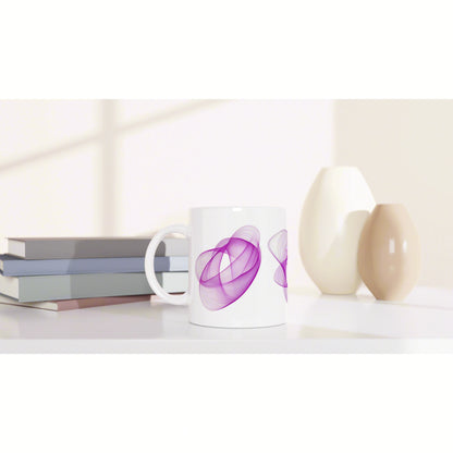 White mug with a purple abstract swirl pattern on a clean desk beside stacked books and cream-beige ceramic vases.