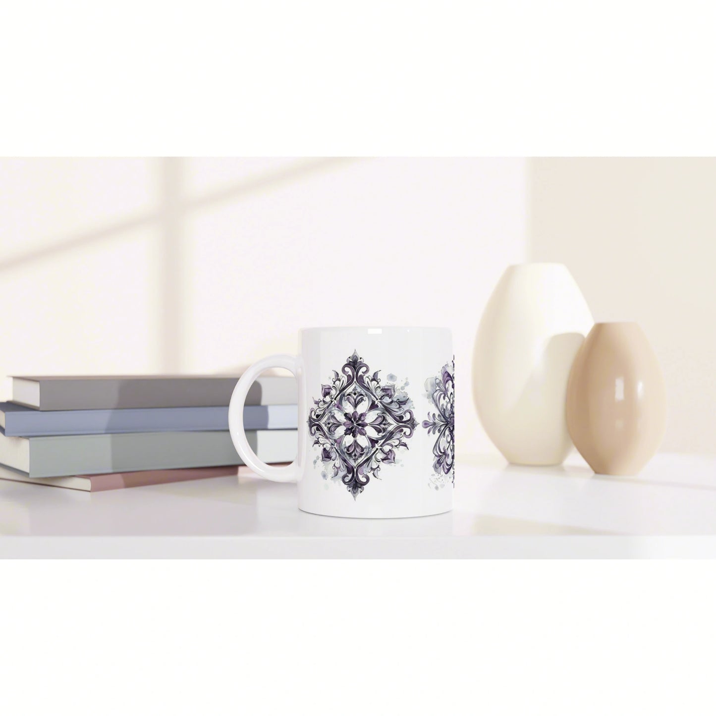 White ceramic mug with a purple ornate damask pattern on a light desk, beside pastel books and decorative vases.