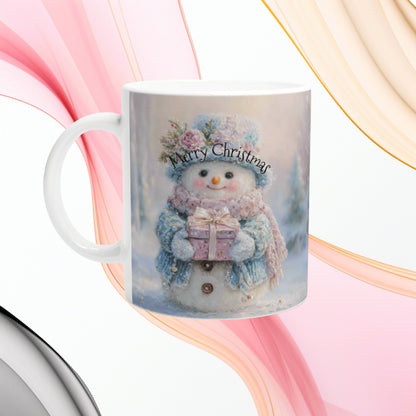 White mug featuring a festive print of a smiling snowman in a pastel scarf, holding a wrapped gift beneath 'Merry Christmas' text.