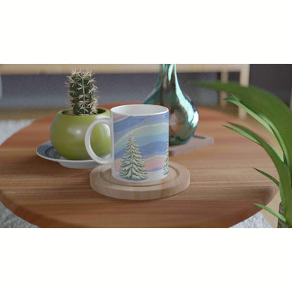 White mug featuring a snowy pine landscape on a pastel sky, placed on a round wooden coaster on a wooden table.