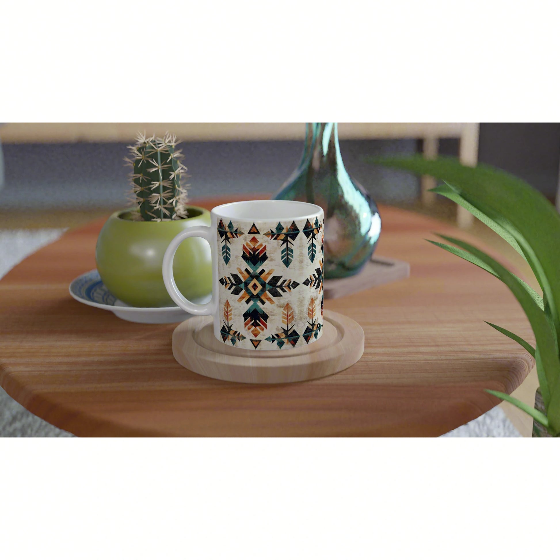 White mug with geometric tribal pattern on a wooden coaster at a table, cactus pot and glass vase in background.