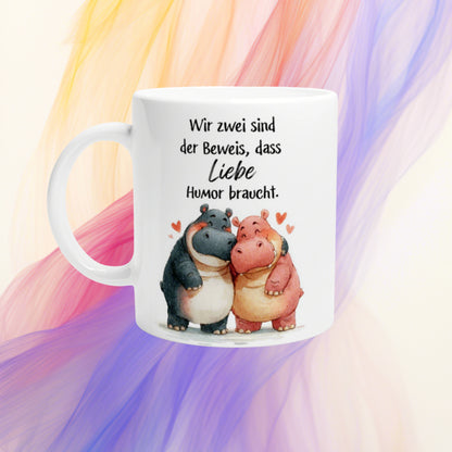 White mug with two hugging hippos and the German caption 'Wir zwei sind der Beweis, dass Liebe Humor braucht'.