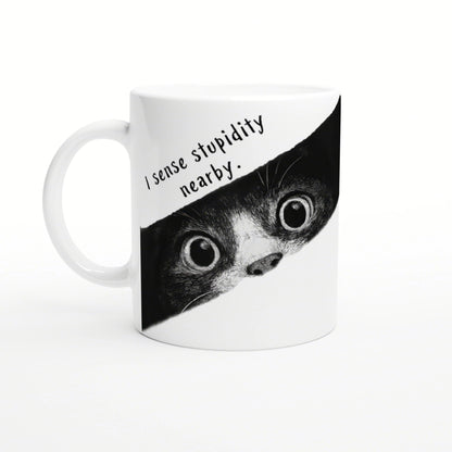 White mug with a black-and-white illustration of a wide-eyed animal peeking from a torn banner that reads I sense stupidity nearby